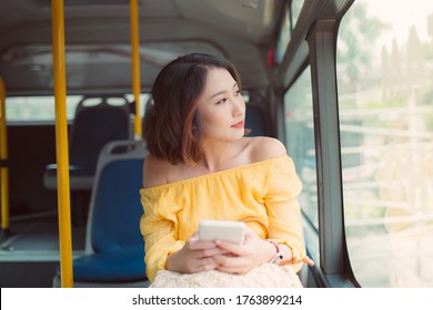 Young Beautiful Woman Holding Mobile Phone And Looking Outside When Sitting On Bus