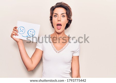 Young beautiful woman holding sad to happy emotion paper scared and amazed with open mouth for surprise, disbelief face 
