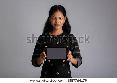 Young beautiful woman holding and showing blank screen of smartphone or mobile or tablet phone on a gray background.