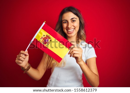 Young beautiful woman holding spanish flag over red isolated background with a happy face standing and smiling with a confident smile showing teeth