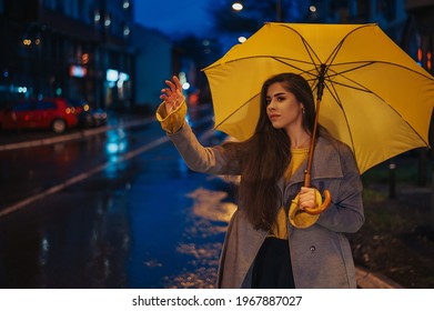 Young beautiful woman holding a yellow umbrella and calling for a cab on a rainy night in the city - Powered by Shutterstock