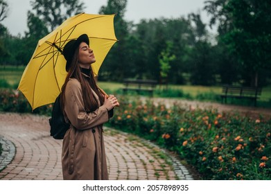 Young Beautiful Woman Holding A Yellow Umbrella And Enjoying A Walk In The Park During Rain