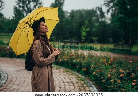 Young beautiful woman holding a yellow umbrella and enjoying a walk in the park during rain
