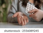 A young beautiful woman holds a pink round contraceptive hormonal pill in her hands. The girl is going to take medicine for headache and stomach ache at home.