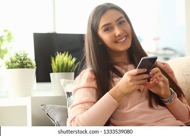 Junge schöne Frau hält Smartphone in der Hand, indem sie zu Hause Kosten über Sofa. Überprüfung interner Informationen Die Freiheit der finanziellen Werbung macht Geldtransfer zum Konzept des Auftragnehmers