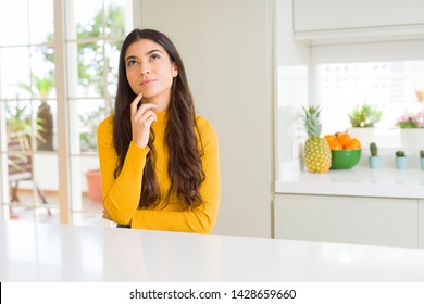 Young Beautiful Woman At Home On White Table With Hand On Chin Thinking About Question, Pensive Expression. Smiling With Thoughtful Face. Doubt Concept.