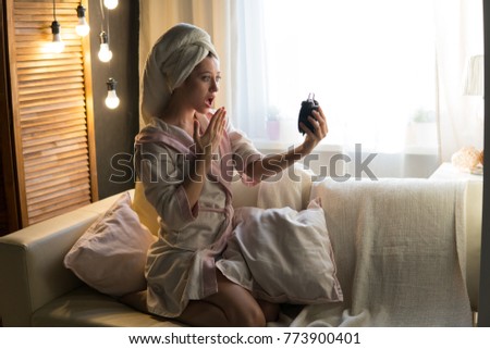 Young beautiful woman in a house dressing gown and with a towel on her head sits on the couch