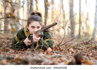 Young beautiful woman hunter in a camouflage aiming from a gun