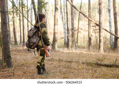 Young beautiful woman hunter with shotgun looking in forest