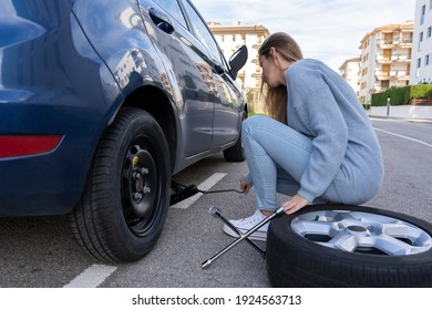 Young Beautiful Woman Jacks Up Her Car To Replacing The Wheel.Changing Winter To Summer Tires Concept,flat Tire Maintenance And Services, Driving Trouble Lifestyle