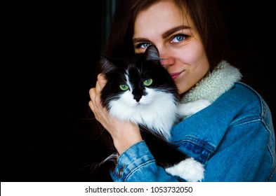 Young Beautiful Woman In A Jeans Jacket Hugs A Black And White Cat