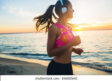 young beautiful woman jogging on beach, morning, fitness outfit, listening to music on headphones, smartphone, sea sunrise, skinny perfect slim body, healthy living lifestyle, summer, smiling, happy - Powered by Shutterstock