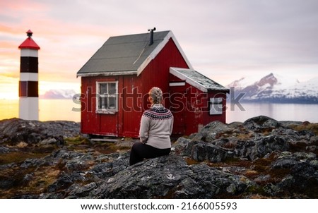 Young beautiful woman in knitted sweater on the shore of sea during sunset or sunrise. Moments of life, enjoying nature. Lyngstuva lighthouse, Lyngen, Lyngenfjord, Troms og Finnmark, Norway