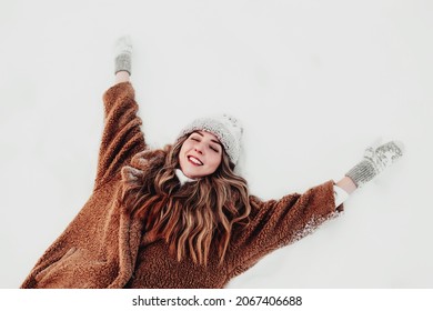 Young beautiful woman laying down on the white snow in the winder forest. Girl is happy with closed eyes. Female has winder vacation and waiting for winter holidays.  - Powered by Shutterstock