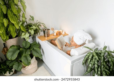 A young beautiful woman lies in a bath with white foam. Reading a book and enjoying a bath. Candles and house plants. The concept of relaxation and harmony. - Powered by Shutterstock