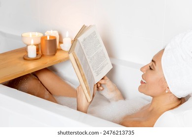 A young beautiful woman lies in a bath with white foam. Reading a book and enjoying a bath. Candles and house plants. The concept of relaxation and harmony. - Powered by Shutterstock