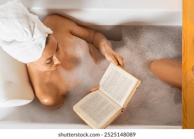 A young beautiful woman lies in a bath with foam and rose petals, reads a book and drinks champagne. The concept of relaxation, rest, self-care, self-love and harmony. Top view. - Powered by Shutterstock