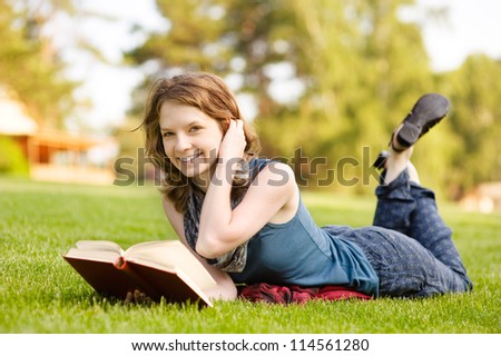 Young beautiful woman lies on green summer meadow with book