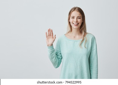 Young beautiful woman with long blonde hair congratulating her friend on her birthday. Pretty student girl saying hello, smiling joyfully and friendly, waving her hand
