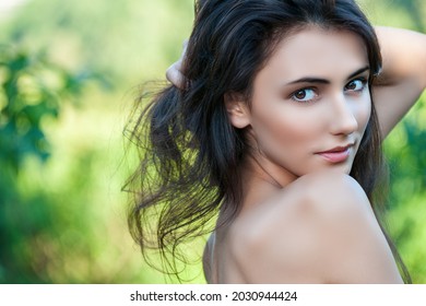 Junge schöne Frau mit langen dunklen Haaren mit nackten Schultern, Nahaufnahme auf dem Hintergrund der Sommergrüne.
