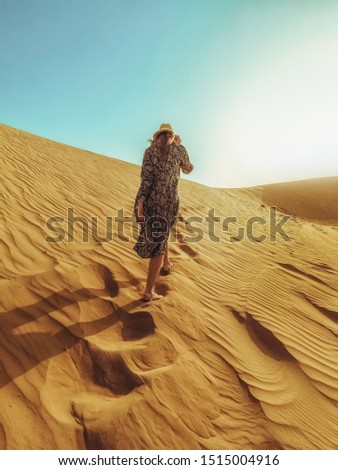 Young beautiful woman in a long dress walks along the sand dunes of the Dubai desert