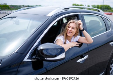 Young beautiful woman with long hair sits in a black car at a parking lot. Pretty girl in casual clothes. Car trip - Shutterstock ID 1960192726