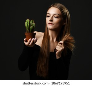 Young beautiful woman with long silky straight hair in black body holding cactus plant in pot and comparing with split ends over dark background. Haircare, beauty, wellness concept