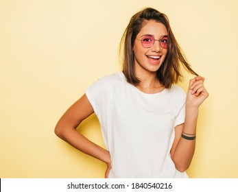 Young beautiful woman looking at camera. In casual summer white T-shirt and jeans shorts in round sunglasses. Positive female shows facial emotions. Funny model isolated on yellow  - Shutterstock ID 1840540216