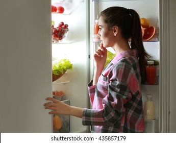 Young beautiful woman looking into fridge at night
