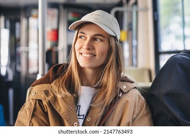 Young beautiful woman looking through the metro train or bus window. Happy bus passenger traveling sitting in a seat and looking through the window. Girl wear beige cap  and brown trench coat. - Powered by Shutterstock