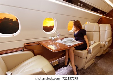 young beautiful woman in Luxury interior in bright colors of genuine leather in the business jet, sky and rays of sunset through the porthole