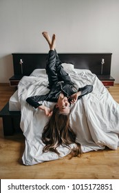 Young beautiful woman lying upside down with legs up on bed with white linen and talking on the phone