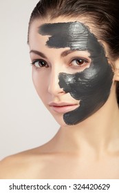 Young beautiful woman in a mask for the face of the therapeutic black clay. Spa treatment.