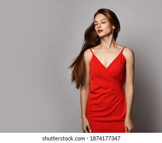 Young beautiful woman model in red dress with long silky straight hair standing with eyes closed over grey background, copy space. Haircare, beauty, wellness, hairstyle concept