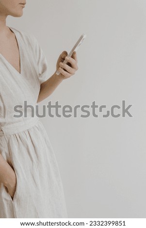 Young beautiful woman in neutral beige creamy linen dress holding mobile phone