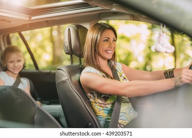 Young Beautiful Woman With A Nice Smile Driving A Car.  Her Cute Daughter Sitting On Rear And Enjoying.