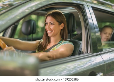 Young Beautiful Woman With A Nice Smile Driving A Car.  Her Cute Daughter Sitting On Rear And Enjoying.