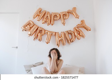 Young Beautiful Woman In Nightie Celebrating Happy Birthday. Morning Surprise In Bad With Rose Gold Balloons. White Linens And Pillows. Party In Bed Concept