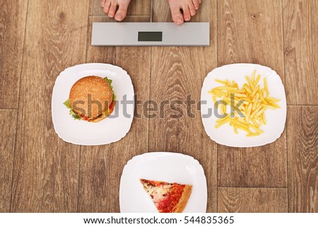 A young beautiful woman is on the scales. To choose between potato chips, pizza and burgers. The concept of healthy eating. Healthy Lifestyle. Diet.