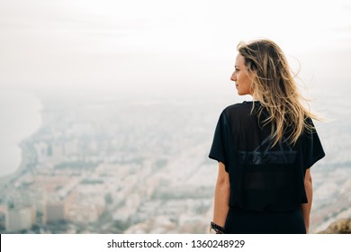Young beautiful woman on top of the mountain looking at the city from above