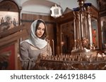 Young beautiful woman in the Orthodox Church lit candles in a candlestick