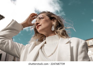 Young beautiful woman outside, stylishly dressed, in jewelry, enjoys the good sunny weather. - Shutterstock ID 2247687739