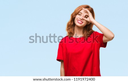 Young beautiful woman over isolated background doing ok gesture with hand smiling, eye looking through fingers with happy face.