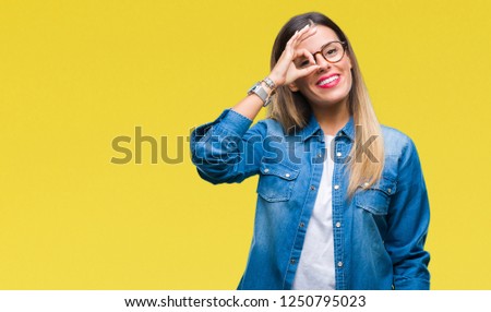 Young beautiful woman over wearing glasses over isolated background doing ok gesture with hand smiling, eye looking through fingers with happy face.