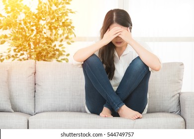 Young Beautiful Woman In Painful Expression Suffering Menstrual Period Pain On Sofa Couch Having Tummy Cramp In Female Health Concept. Lifestyle And Health Concept Mixed Race Asian Chinese Model.