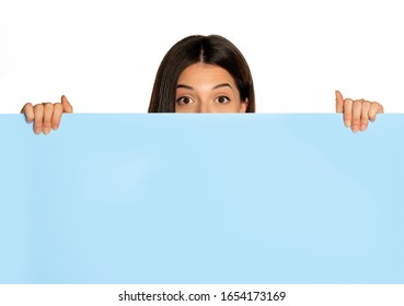 young beautiful woman peeking behind a blue empty board on white background