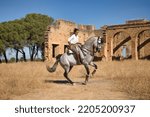 Young beautiful woman performing turns riding her horse in the countryside next to an abandoned and ruined building on a sunny day. Concept horse riding, animals, dressage, horsewoman.