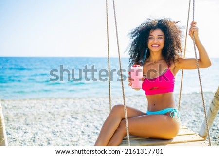 Young beautiful woman with pink milk shake on the beach chilling on swing alone