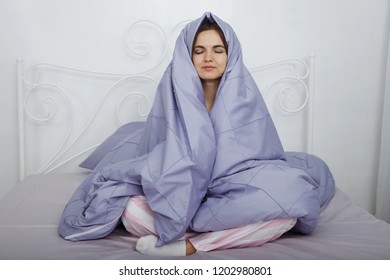 Young Beautiful Woman In Pink Pajamas Is Sitting With A Blanket Over Her Head In Bed With Blue Bedclothes.