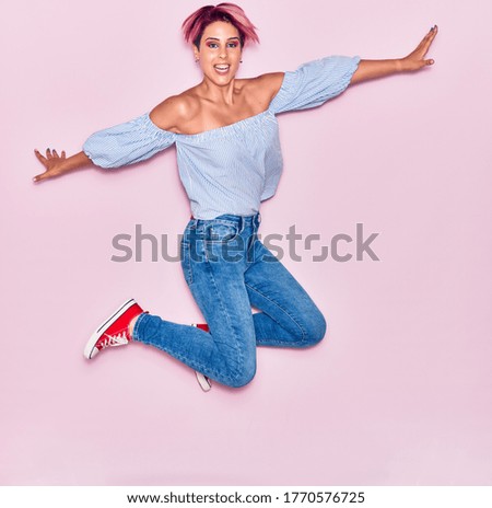 Young beautiful woman with pink short hair wearing casual clothes smiling happy. Jumping with smile on face and open arms over isolated background.